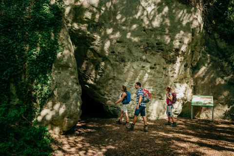 A group of hikers passes by a large rock. In the background, a directional sign can be seen.