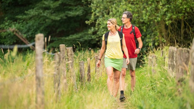 Een koppel wandelt over een smal pad door een groen, bebost landschap.
