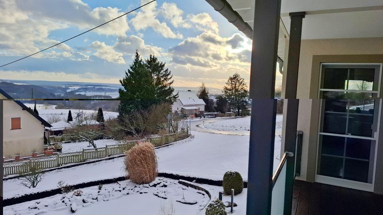 Eine winterliche Landschaft mit frisch gefallenem Schnee und einem klaren Himmel. Im Hintergrund sind Häuser und Bäume zu sehen.