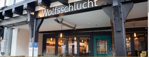 Ein modernes Restaurant namens Wolfschlucht mit einer einladenden Fassade. Die Fenster sind groß und zeigen eine stilvolle Innenausstattung.