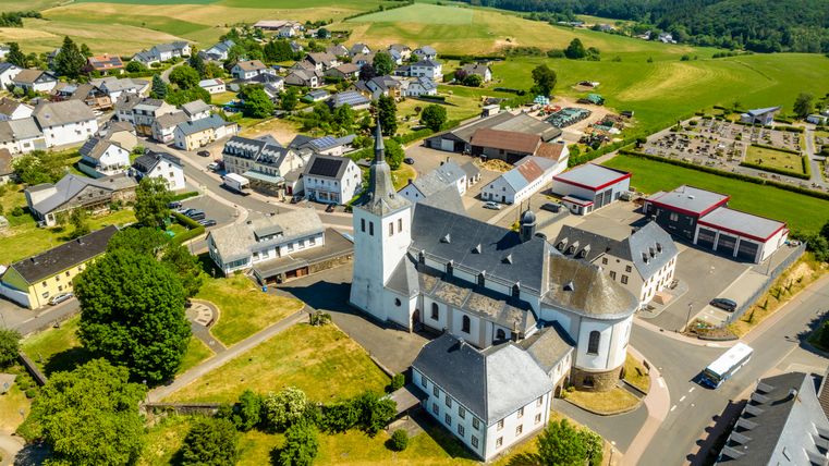 Luchtfoto van Bleialf met kerk en omliggende gebouwen.