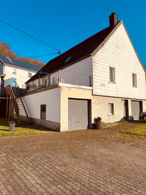 Een modern huis met een lichte gevel en een balkon. De tuin is goed onderhouden en de omgeving is helder en zonnig.