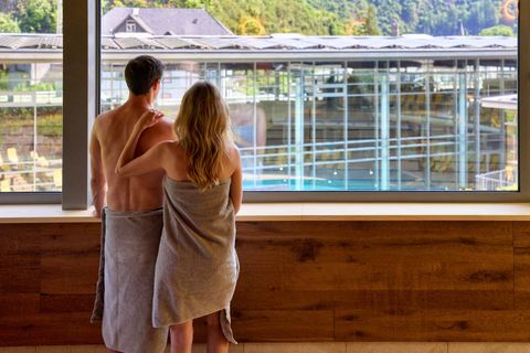 Eine Gruppe von Menschen macht Wassergymnastik in einem hellen Schwimmbad. Im Hintergrund sind große Fenster und ein angenehmes Ambiente zu sehen.