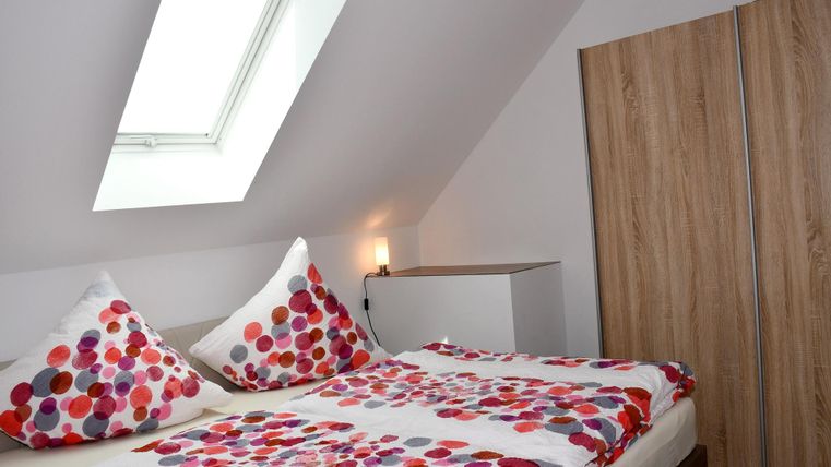 A cozy bedroom with a double bed and colorful cushions. There is a wardrobe and a skylight that lets in natural light.