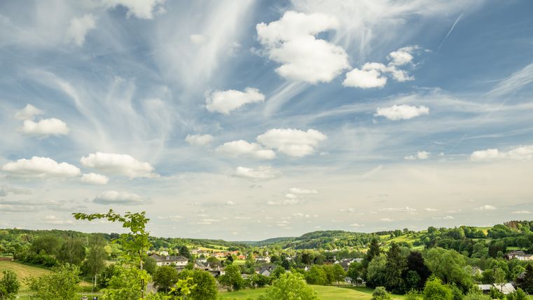 Paysage avec des champs verts, des arbres et un village sous un ciel bleu avec des nuages blancs.