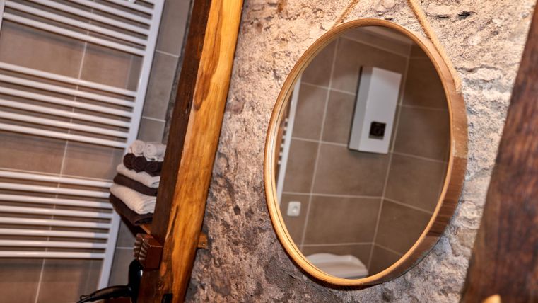 Ein modernes Badezimmer mit einem runden Spiegel und einer Steinwand. Handtücher liegen ordentlich bereit und ein Heizkörper ist sichtbar.