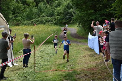 Un groupe d'enfants participe à une course, tandis que des spectateurs se tiennent au bord et prennent des photos. Plusieurs enfants courent sur un chemin de campagne, et une partie des spectateurs est en admiration.