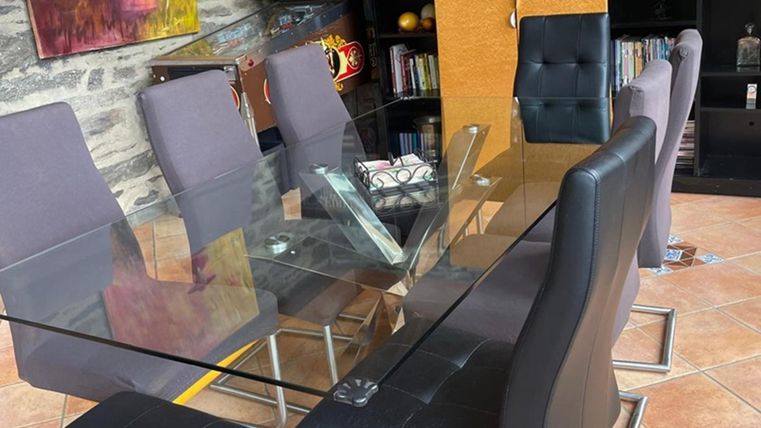 An elegant dining area with a glass table and black chairs. In the background, bookshelves and decorative elements are visible.