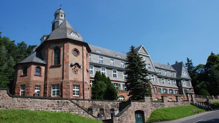 Ein historisches Gebäude mit markanten Türmen und einer schönen Fassade. Umgeben von grünen Bäumen und einem klaren blauen Himmel.