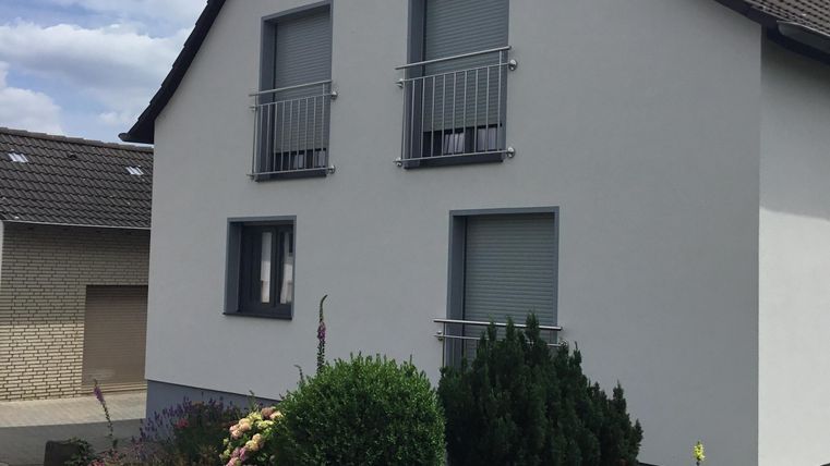 A modern, white house with two balconies and a well-kept garden. The surroundings are quiet and inviting.