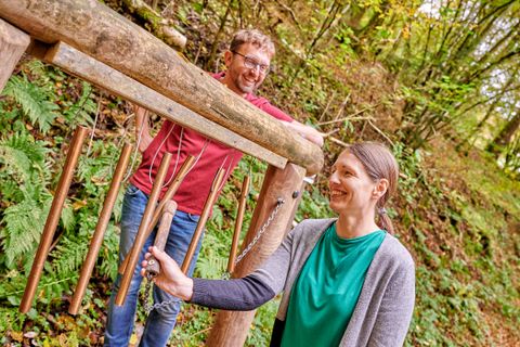 Twee mensen bij een houten klokkenspel in het bos.