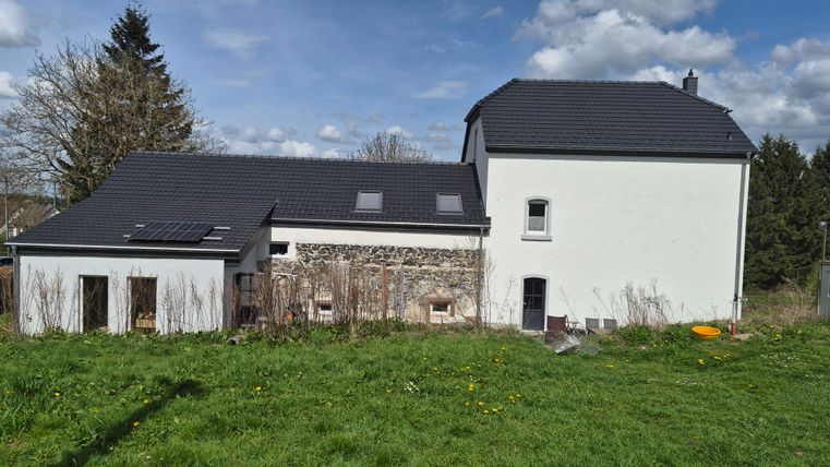 Een modern huis met een plat dak en een stenen gevel. De tuin is groen en omgeven door weilanden.