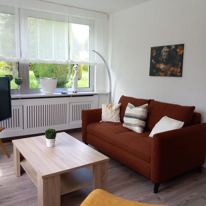 Een gezellige woonkamer met een bruine bank en een houten tafel. De grote ramen bieden veel licht en uitzicht op de tuin.