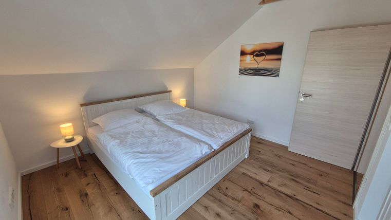 Une chambre lumineuse avec un grand lit et un sol en bois. Sur le mur, il y a une image avec un motif de cœur.