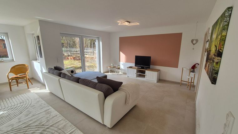 Un salon moderne avec un canapé blanc et une télévision. De grandes fenêtres laissent entrer beaucoup de lumière naturelle.