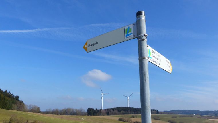 Panneau indicateur à la source de la Lieser avec des éoliennes en arrière-plan.
