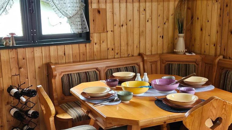 A cozy dining area with a wooden table and colorful plates. The walls are made of wood, and there is a window view with curtains.