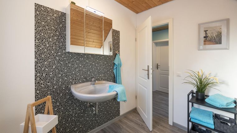 Een modern badkamer met een rond wastafel en een stijlvolle spiegel. De muren zijn versierd met een stenen patroon en er zijn frisse handdoeken in verschillende tinten blauw.