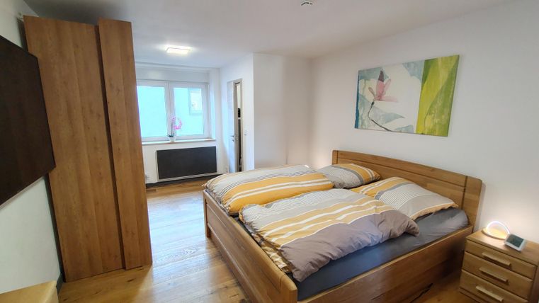 Een gezellige slaapkamer met een houten bed en kleurrijke beddengoed. De kamer heeft een moderne stijl en grote ramen die voor daglicht zorgen.