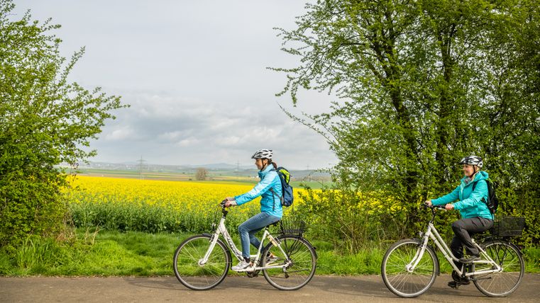 Twee fietsers op een pad naast een bloeiend koolzaadveld.