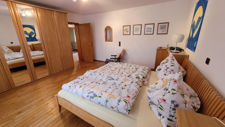 Ein gemütliches Schlafzimmer mit einem großen Bett und Blumenbettwäsche. An der Wand hängen Bilder und es gibt einen Kleiderschrank aus Holz.