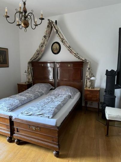Ein gemütliches Schlafzimmer mit einem Doppelbett aus Holz und einer eleganten Bettdecke. Die Wände sind schlicht, und ein Kronleuchter sorgt für angenehmes Licht.