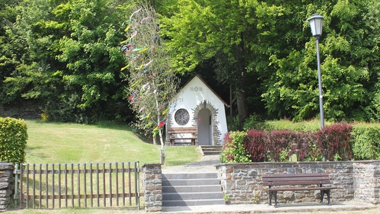 Een klein, charmant kerkje staat omgeven door groene bomen. Op de weide ervoor nodigt een bankje uit om te vertoeven.