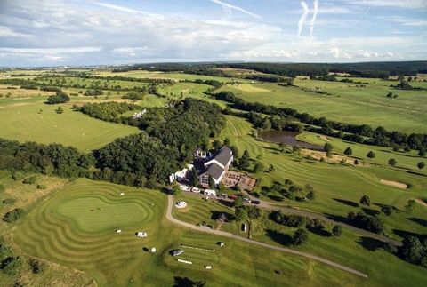 Un paysage de douces collines et un terrain de golf. En arrière-plan, un bâtiment accueillant et un petit étang.