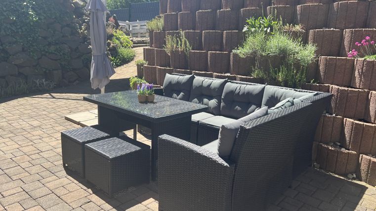 Een gezellige zithoek van riet met een tafel en parasol. De vloer is met stenen bestraat en er zijn planten op de achtergrond.
