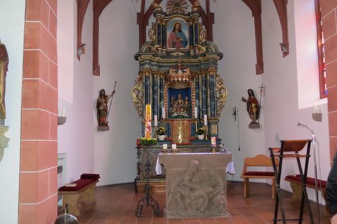 Ein schöner Kircheninnenraum mit einem kunstvoll gestalteten Altar. Die Wände sind geschmückt und es gibt Holzstatuen neben dem Altar.