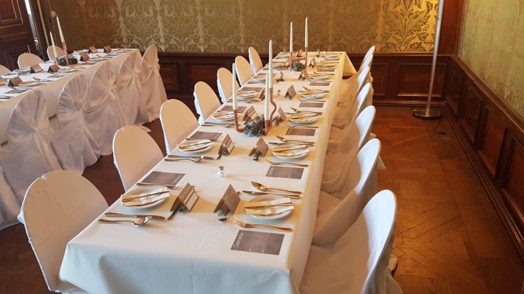 Ein elegant gedeckter Tisch in einem festlichen Raum. Die Tische sind mit weißen Tischdecken, Besteck und Kerzen dekoriert.