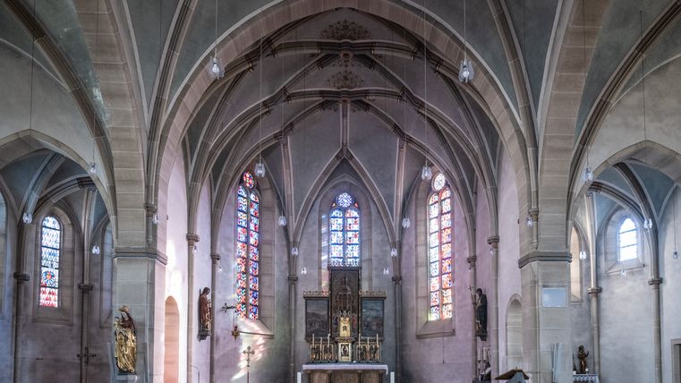 Binnenaanzicht van een kerk met gotische bogen en kleurrijke gebrandschilderde ramen.