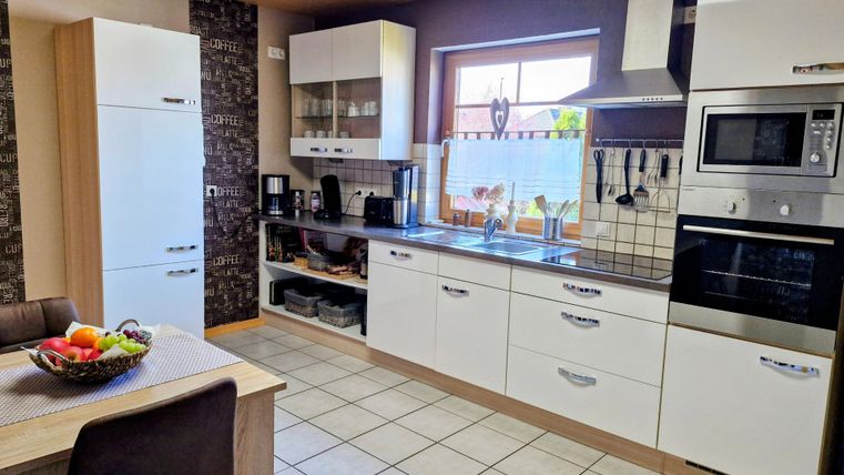 Een moderne keuken met witte kasten en een werkblad van roestvrij staal. Op de tafel staat een schaal met vers fruit.