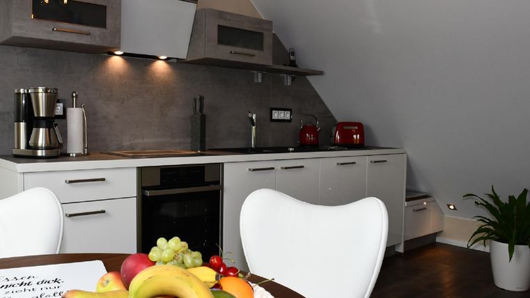 A modern kitchen with white cabinets and an elegant countertop. On the table, there is a fruit bowl with various fruits.