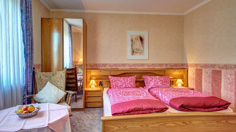 Ein gemütliches Schlafzimmer mit zwei Betten und rosa Bettwäsche. Der Raum hat einen Spiegel, einen Tisch mit einem Obstkorb und warmes Licht von den Nachttischlampen.