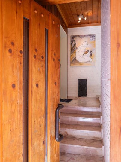 Un hall d'entrée accueillant avec des portes en bois et un escalier menant à l'étage. Un ouvrage d'art dans des couleurs douces est accroché au mur.