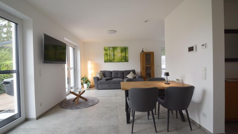 Eine moderne Wohnküche mit einem gemütlichen Sofa und einem Esstisch. Helle Wände und große Fenster sorgen für viel Licht.