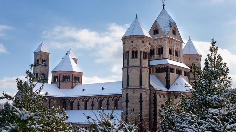 Een indrukwekkende kerk met torens en een met sneeuw bedekt dak. Omringd door dennenbomen in de winter.