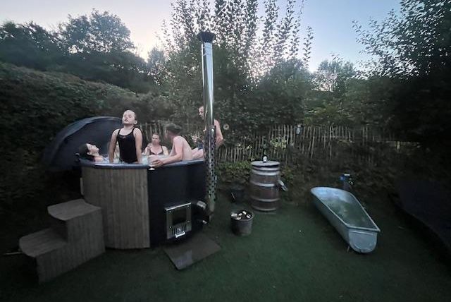 Un groupe de personnes se détend dans un jacuzzi en plein air. Entouré d'arbres verts et d'une ambiance de jardin paisible.