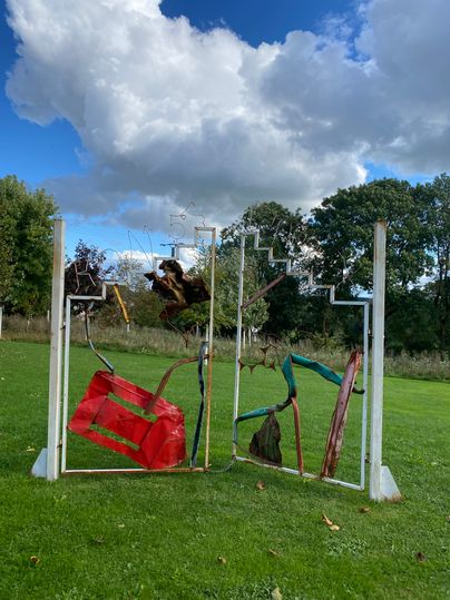 Sculpture en métal sur une prairie avec des nuages en arrière-plan.