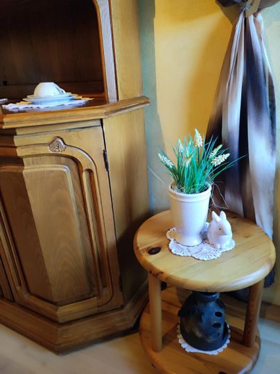 A decorative wooden cabinet with a white cup and a saucer. Next to a small table are a plant and a ceramic figure of a rabbit.