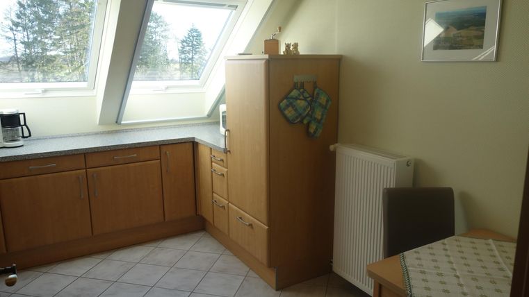 A bright kitchen with wooden cabinets and windows that let in plenty of light. A table and a chair are placed in the corner.