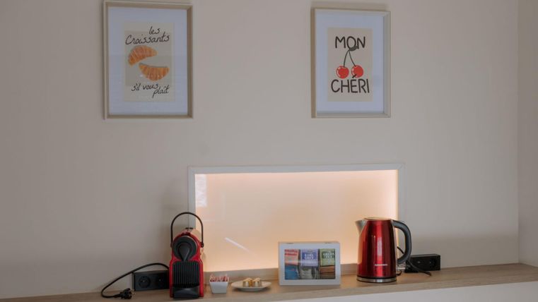 A cozy nook with a kettle, a coffee maker, and a small selection of teas. Two pictures with French inscriptions hang on the wall.