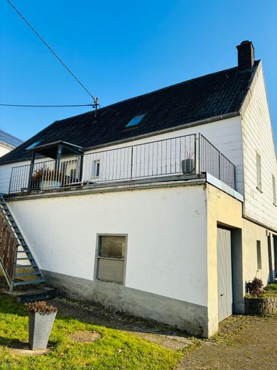 Een modern huis met een schuin dak en een balkon. De gevel is deels wit en er is een klein tuingebied.