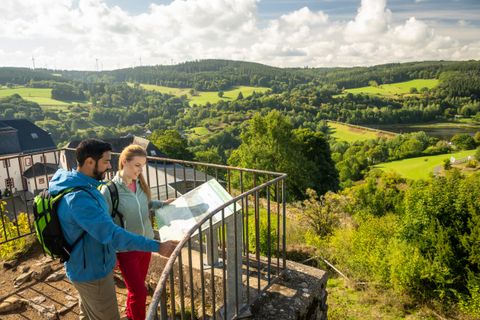 Deux personnes regardent une carte sur une plate-forme d'observation avec vue sur un paysage verdoyant.