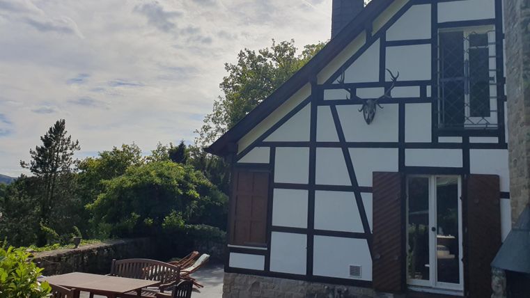 Une charmante maison à colombages avec des fenêtres en bois. Dehors, il y a une terrasse confortable avec des meubles de jardin et une vue sur la nature.