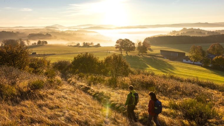 Deux randonneurs sur un sentier dans un paysage vallonné au lever du soleil.