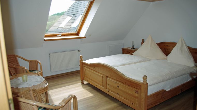 Ein gemütliches Schlafzimmer mit einem Doppelbett und zwei Stühlen. Große Dachfenster sorgen für viel Tageslicht.