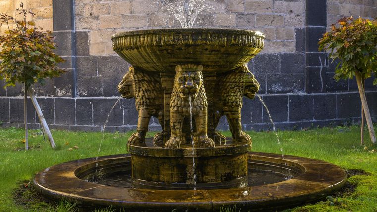 Een mooie fontein met leeuwfiguren. Water spuit uit de fontein en omringt groen gras.