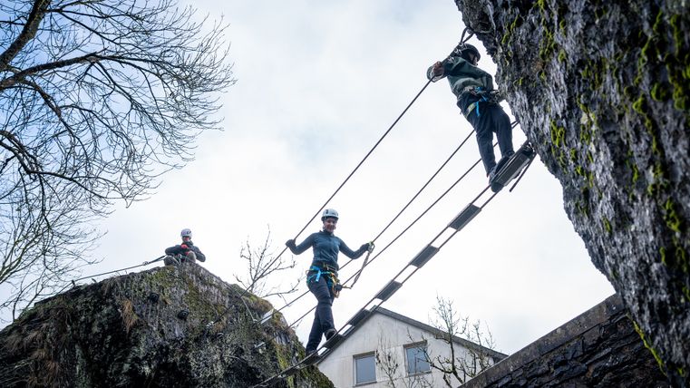 Zwei Kletterer gehen zwischen zwei Felsen über eine Hängebrücke.